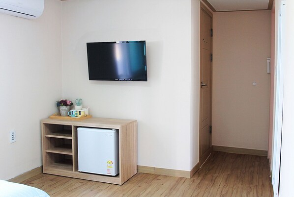 A small room with a white wall-mounted TV, a wooden cabinet with a small fridge, and a door leading to another room. - Our House (Seoul)