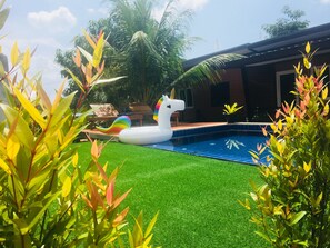 A swimming pool with artificial grass, a white unicorn float, and tropical plants. - At Thara Aonang (Krabi)