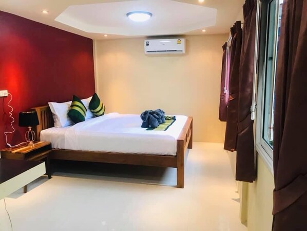 A bedroom with a bed, bedside table, lamp, air conditioning unit, and curtains. - At Thara Aonang (Krabi)