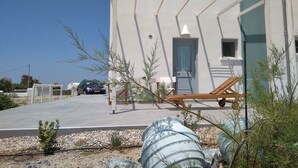 Un moderno edificio blanco con techo curvo, un ventanal pequeño y una puerta con cortina. Se ve una silla de descanso y un coche estacionado adelante.