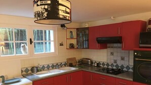 A kitchen with red cabinets, a white sink, a stove, and a window with a cat outside. - Charming T2 garden with trees and parking, close to beaches and golf course. (Seignosse)