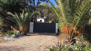 A gated property with a gravel driveway, surrounded by various trees and shrubs. - Charming T2 garden with trees and parking, close to beaches and golf course. (Seignosse)