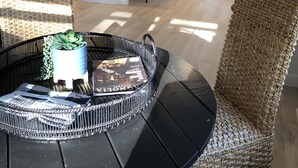 Une cuisine moderne avec des meubles blancs, un îlot central doté de tabourets de bar et un coin repas avec une table noire et des chaises en osier.