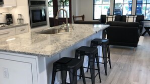 Une cuisine moderne dotée d’un grand îlot central, de tabourets de bar noirs et d’un coin repas avec un canapé et des fauteuils.