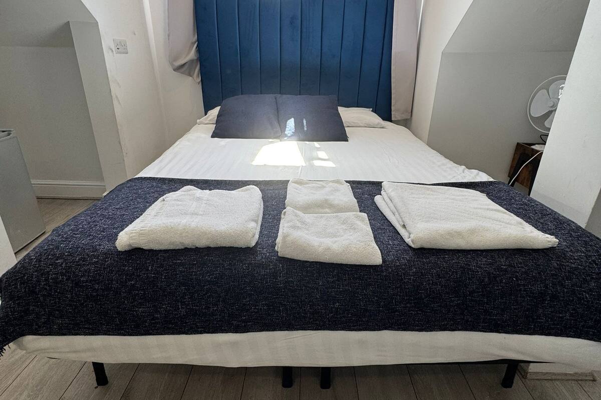 A bedroom with a bed, a blue headboard, and a window with curtains.