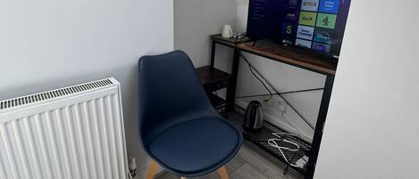 A small room with a white radiator, a blue chair, and a computer desk with a monitor displaying a TV guide.