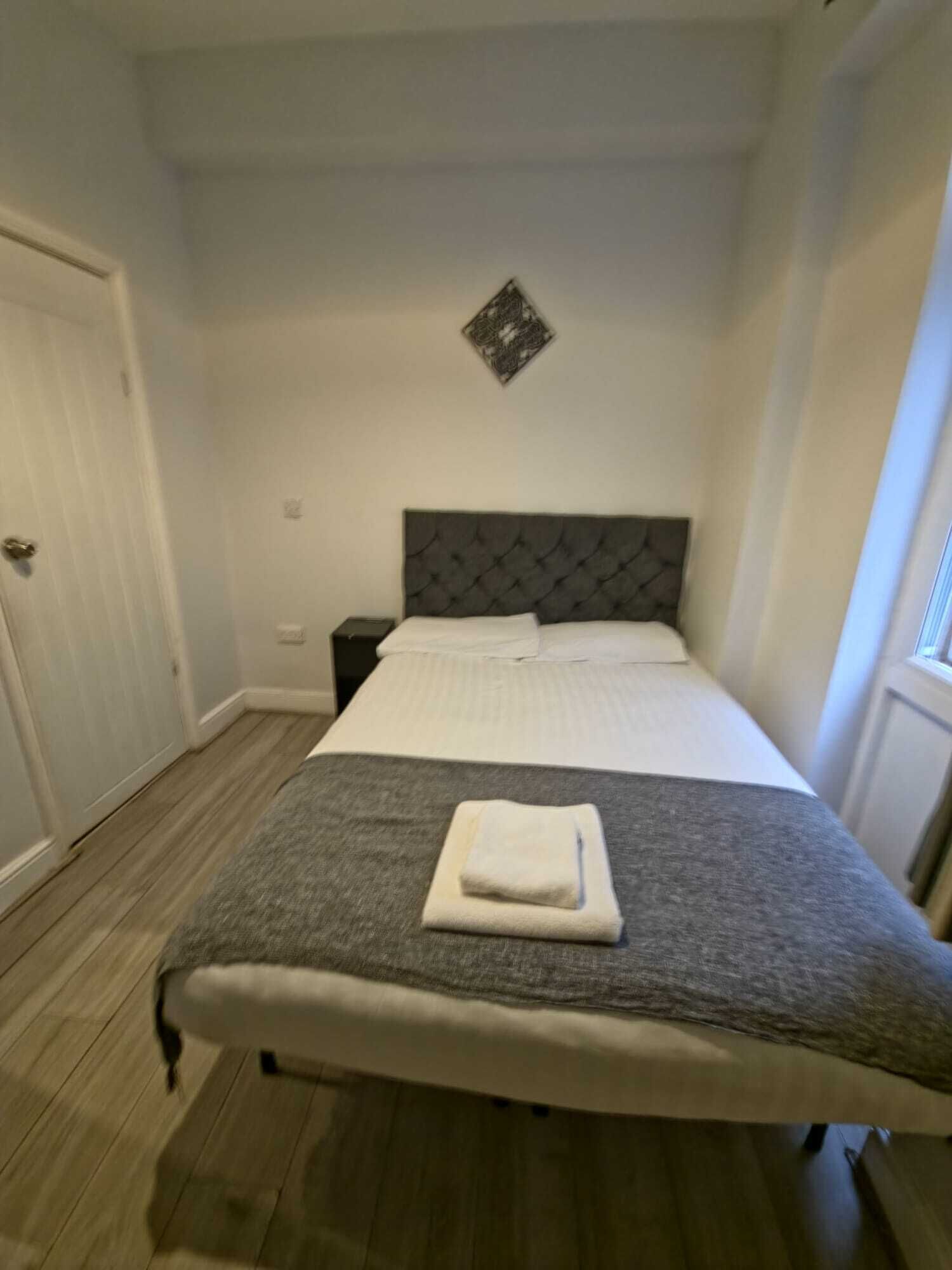 A neatly made bed with a grey and white duvet, a folded white towel, and a dark headboard.