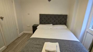 A neatly made bed with a grey and white duvet, a folded white towel, and a dark headboard.