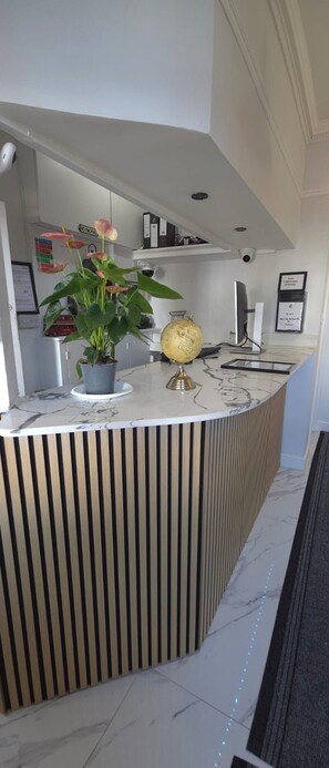A reception desk with a potted plant, a globe, and a computer monitor. - Golders Park Hotel (London)