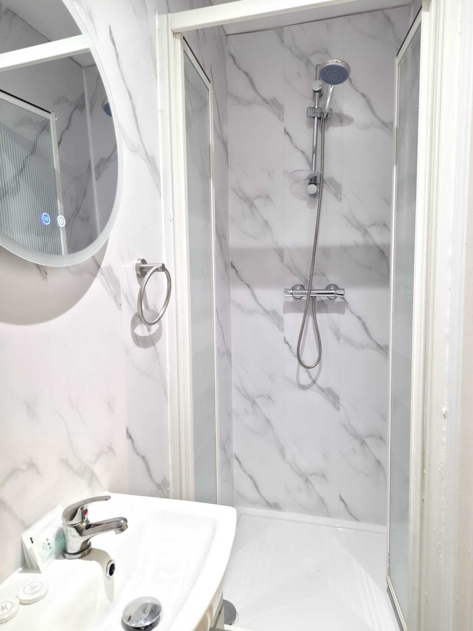 A bathroom with a marble wall, a round mirror, a sink with a faucet, and a shower area with a handheld showerhead.