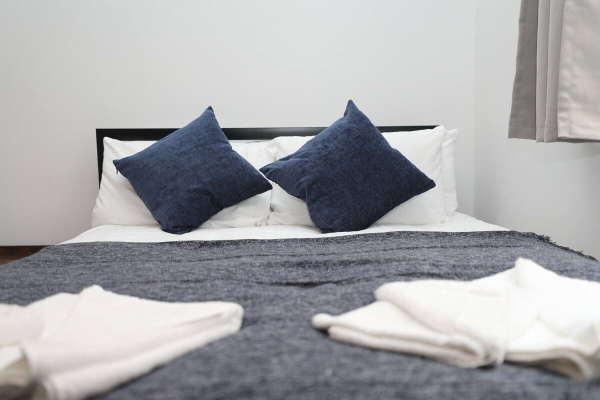 A bed with white linens, two dark blue pillows, and a gray blanket.
