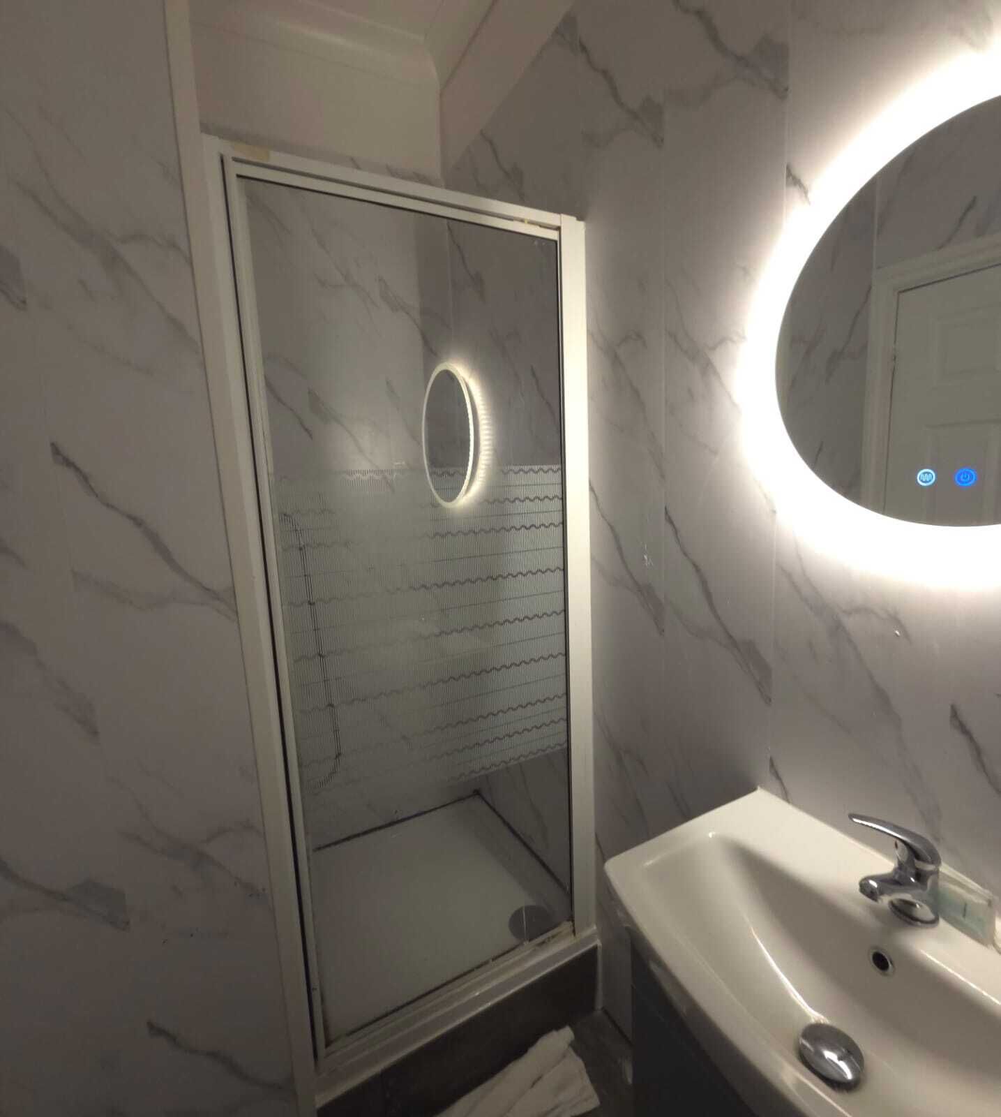 A bathroom with a glass shower enclosure, a marble wall, and a sink with a mirror.