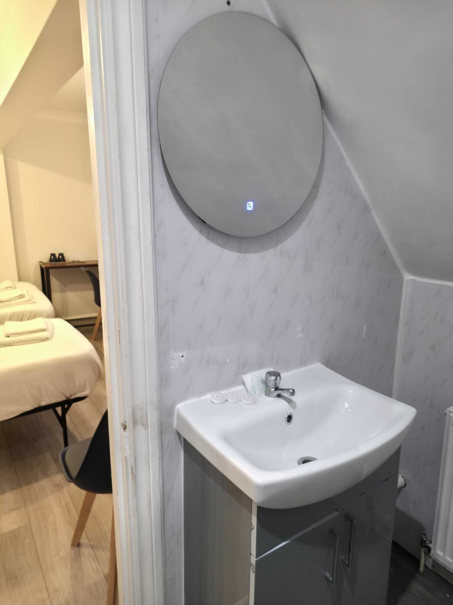 Een badkamer met een ronde spiegel, een witte wastafel en een handdoekhouder.