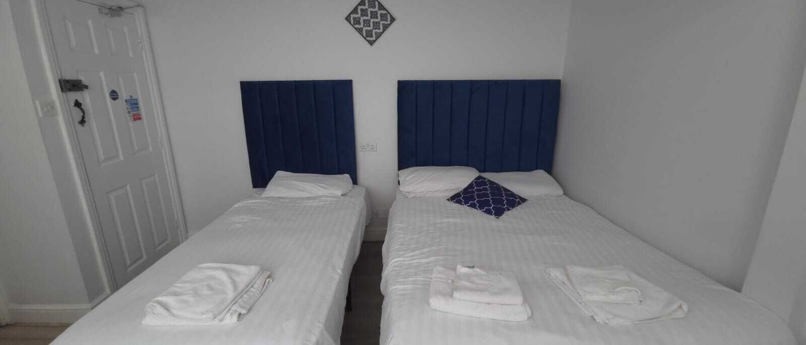 A room with two single beds, each with a blue headboard and white bedding. There are towels on each bed.