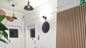 A lobby with a marble floor, two green armchairs, a round table, a clock, and a wooden panel wall. - Golders Park Hotel (London)
