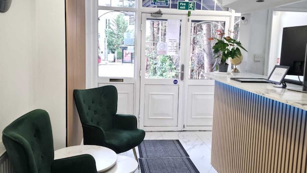 A reception area with a marble floor, green upholstered chairs, a small table, a reception desk, and a pendant light. - Golders Park Hotel (London)
