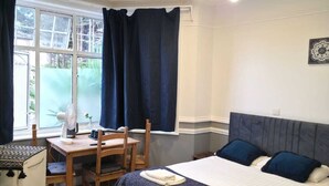 A small, well-lit bedroom with a bed, bedside table, chair, and a desk with a chair. - Golders Park Hotel (London)