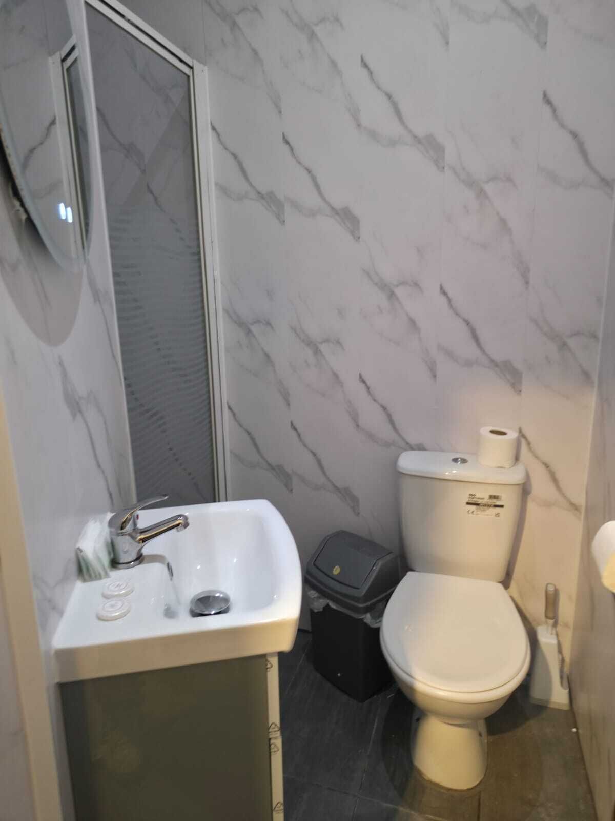 Une salle de bain avec un mur décoré d’un motif imitant le marbre, un lavabo avec un robinet, des toilettes et une poubelle.