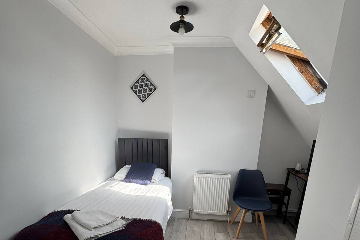 A bedroom with a bed, a chair, a radiator, and a skylight.