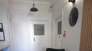 A hallway with a dark rug, two green armchairs, a small round table, and a wall clock. - Golders Park Hotel (London)