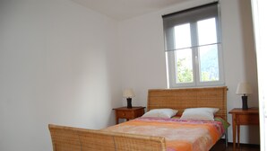 Une chambre à coucher avec un lit, deux tables de chevet, une fenêtre et une vue sur la verdure.