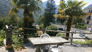 Une table et des chaises en pierre sont disposées sur une surface pavée de pierres, offrant une vue sur une montagne et des arbres.