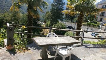 Une table et des chaises en pierre sont disposées sur une surface pavée de pierres, offrant une vue sur une montagne et des arbres.