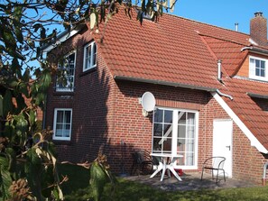 Une maison à deux étages, avec un toit recouvert de tuiles rouges, une antenne parabolique et un petit patio comprenant une table et des chaises.