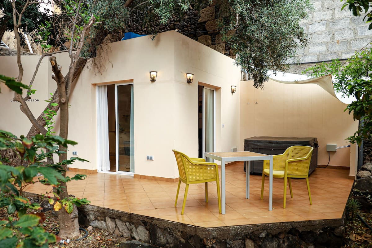 Un patio con una mesa, sillas, un muro de piedra y un árbol.