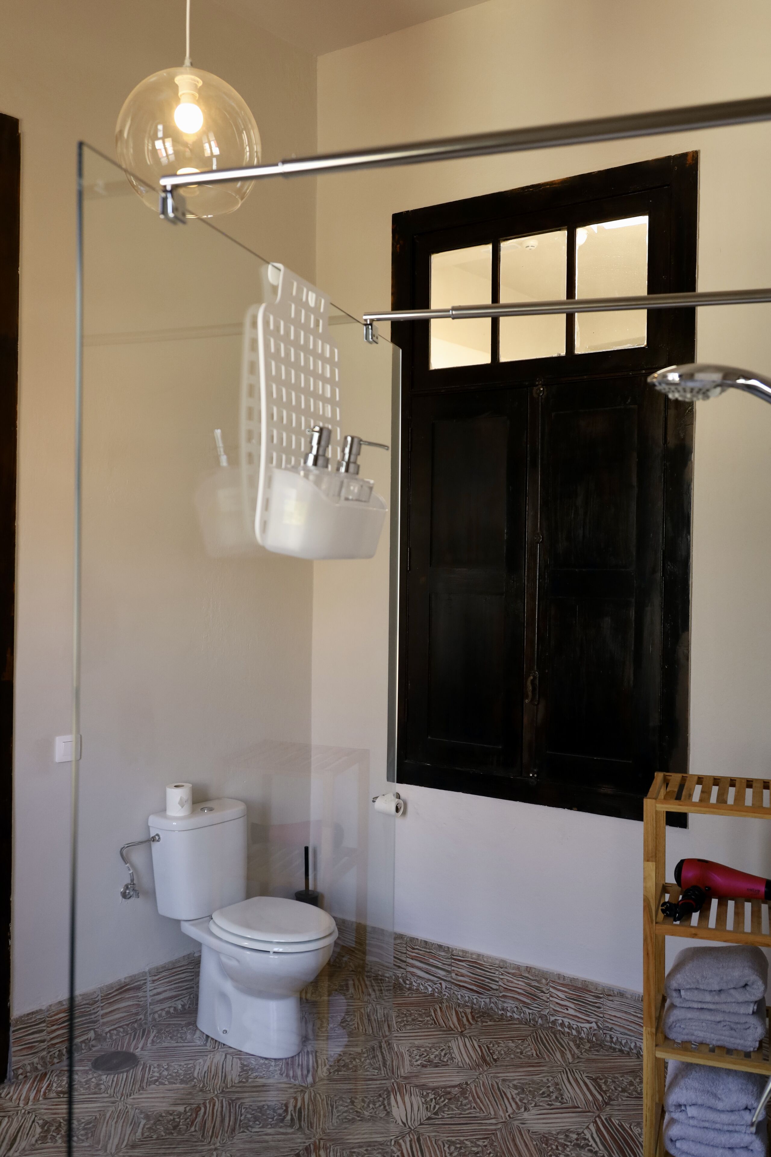 Un baño con inodoro, cabina de ducha de vidrio, toallero y ventana con marco negro.