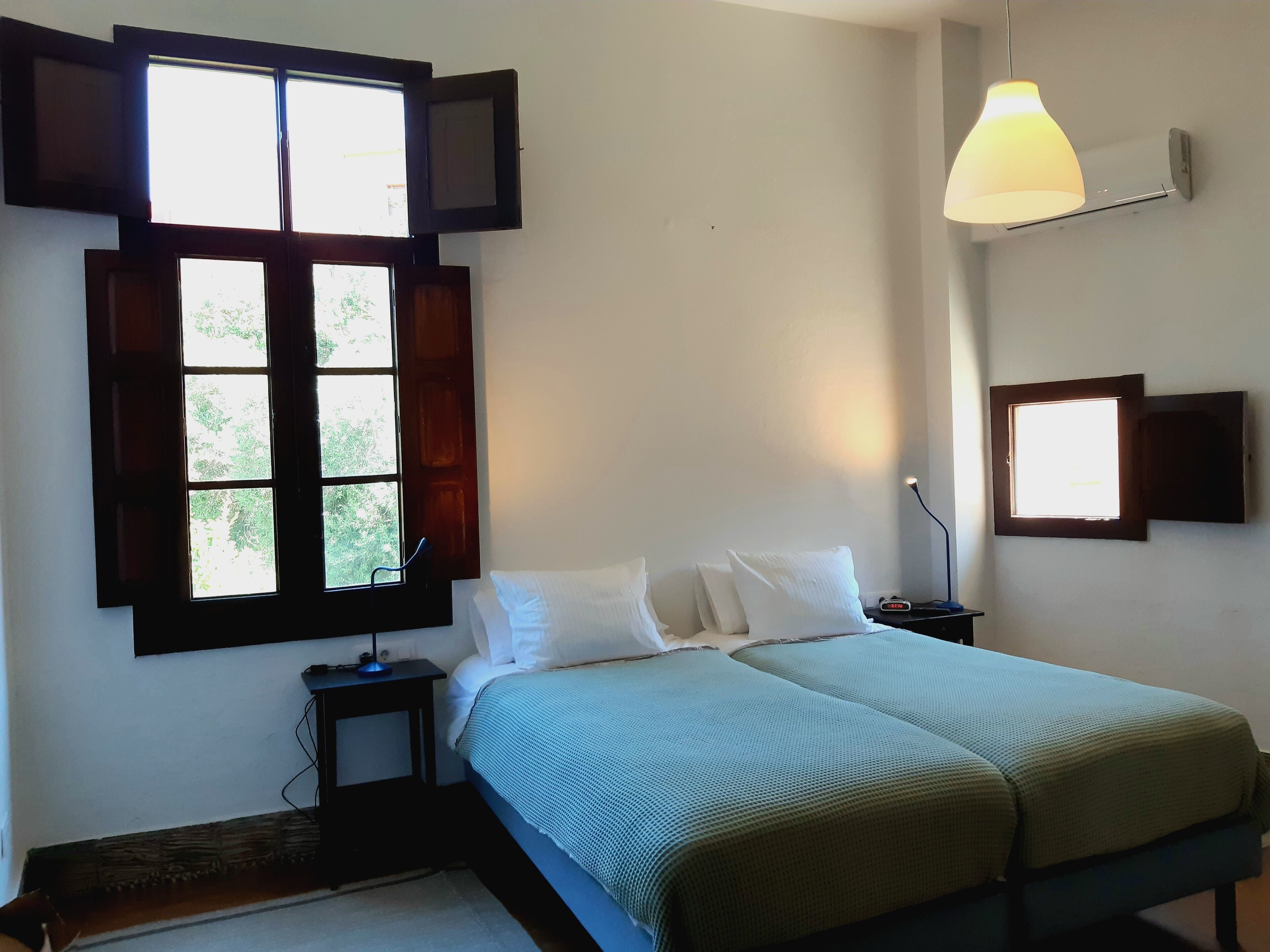 A bedroom with a bed, a nightstand, a lamp, and a window with shutters.