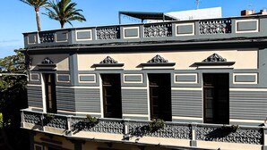 A two-story building with a balcony, a sign indicating 'Villa Nestor', and a palm tree in the background. - Villa Nestor (Ingenio)