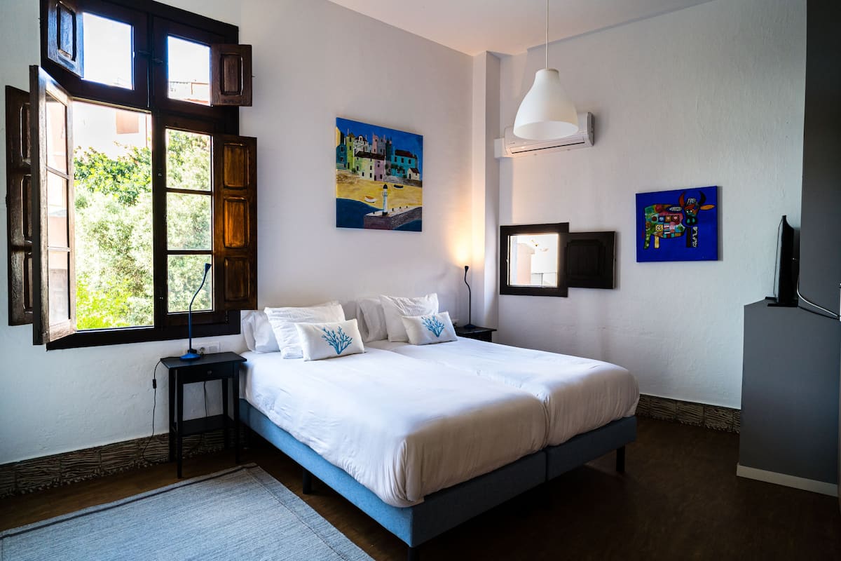 Un dormitorio con cama, mesita de noche, ventana y decoración en la pared.