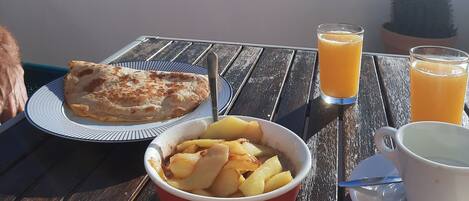 A table with breakfast items including a plate of food, a bowl of fruit, and two glasses of orange juice, with a view of the sky and palm trees in the background.