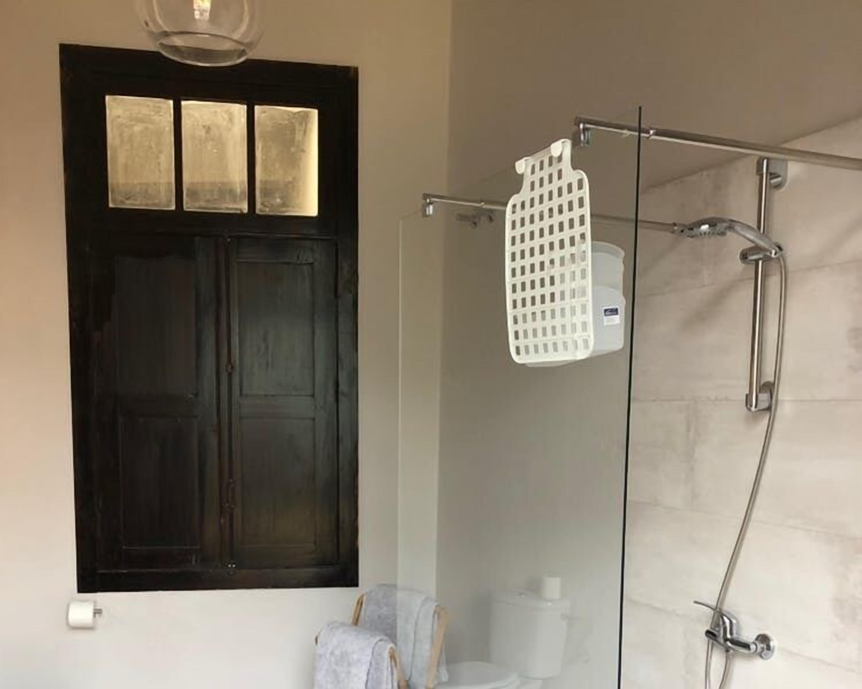 A bathroom with a dark wooden door, a shower with a white plastic shelf, and a toilet.