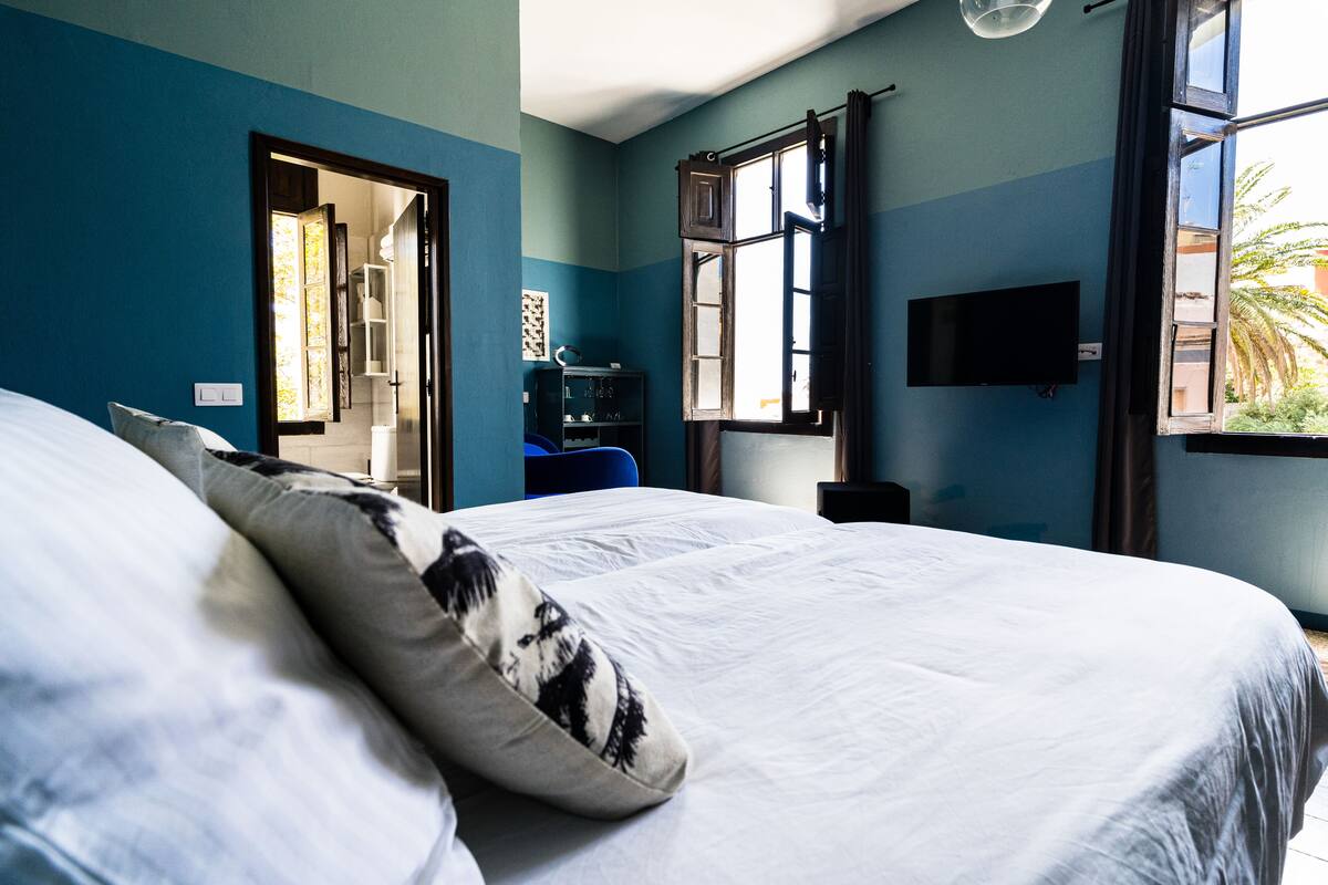 Un dormitorio con una cama grande, un televisor montado en la pared y una ventana con vistas al exterior.
