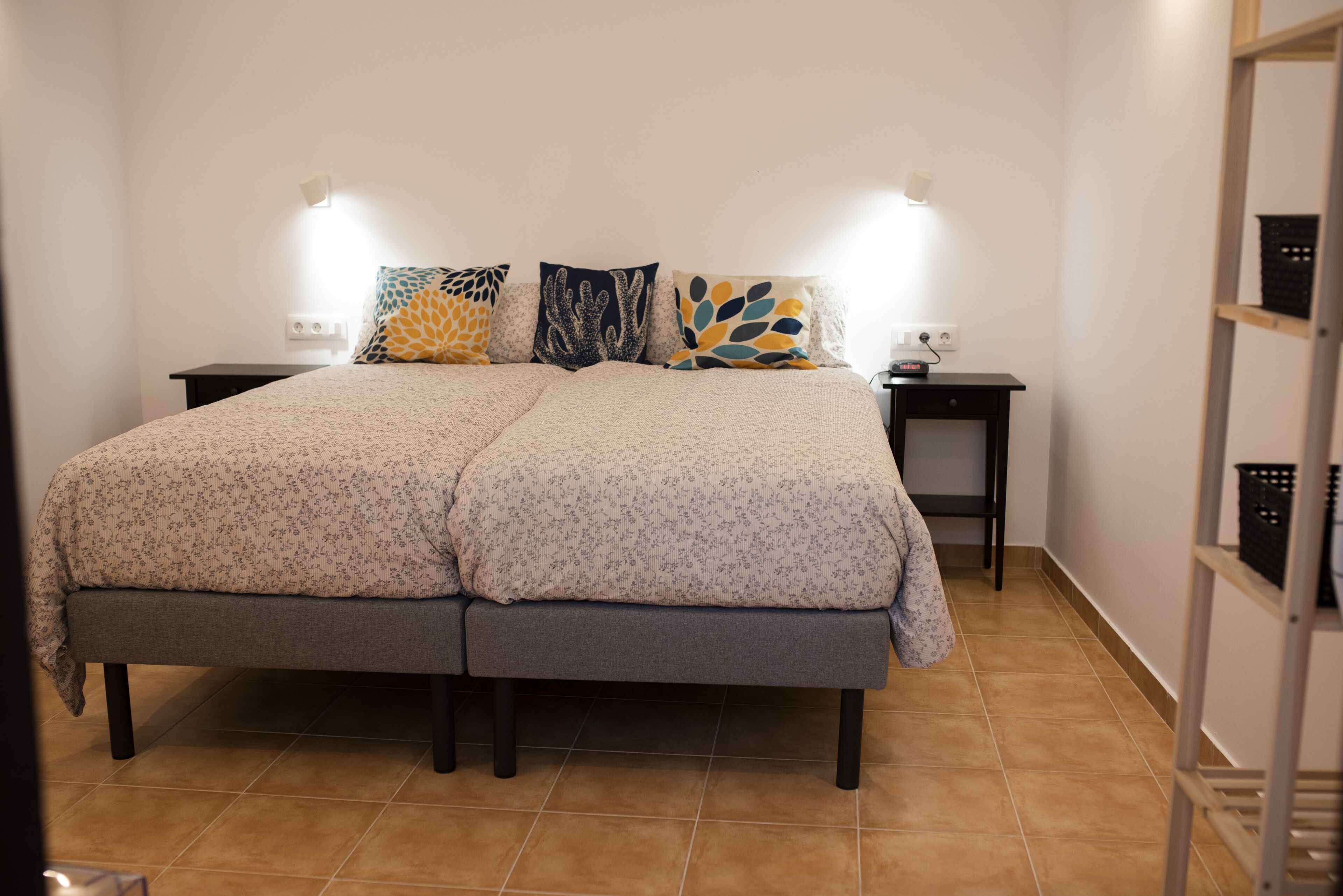 Ein Doppelbett mit blumigem Bettbezug, zwei Nachttische und Wandleuchten.
