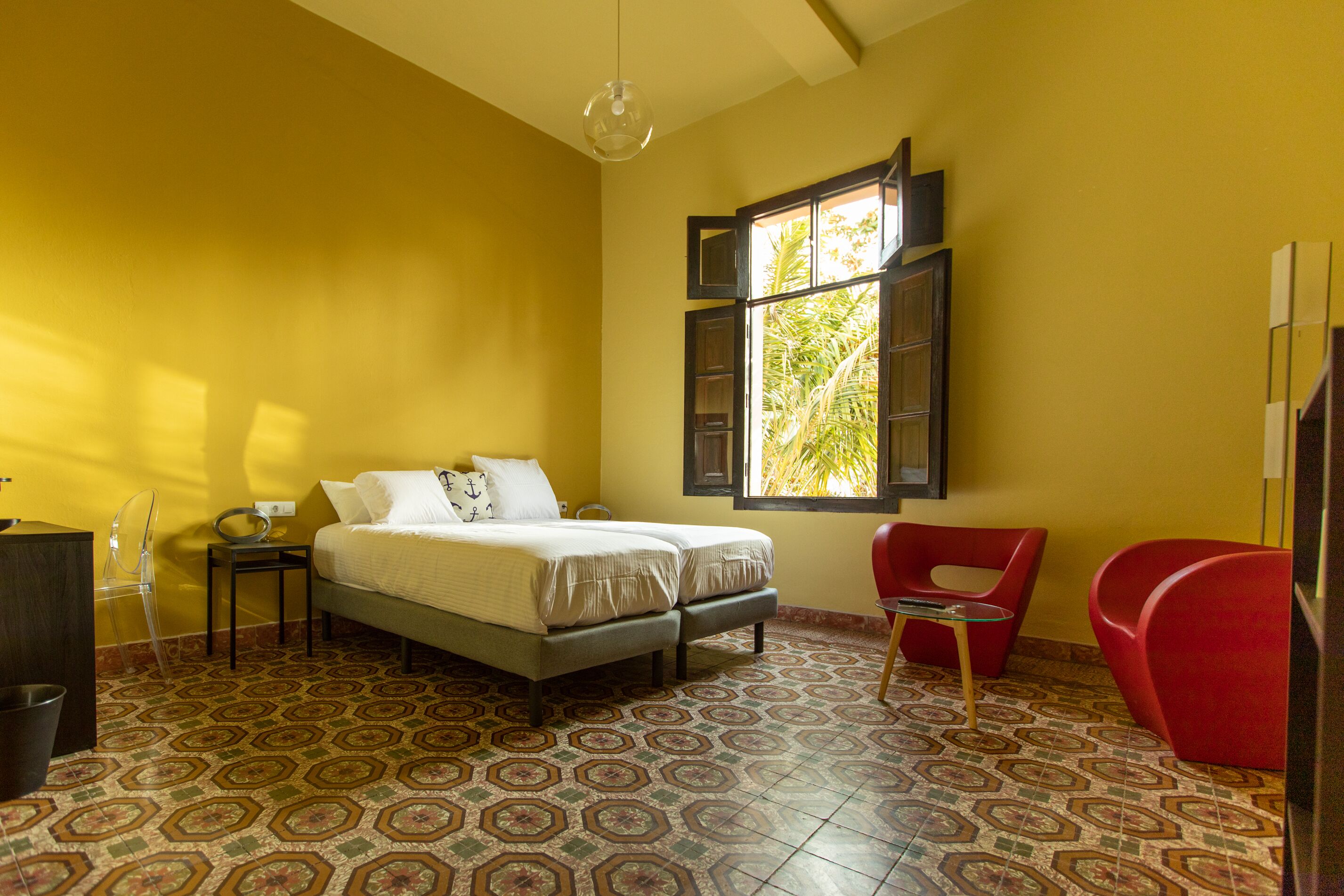 Una habitación con cama, una silla, una mesita y una ventana que da a zonas verdes.