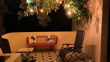 An outdoor patio with a star-patterned tiled floor, a red sofa, a black folding chair, and string lights hanging from a tree.