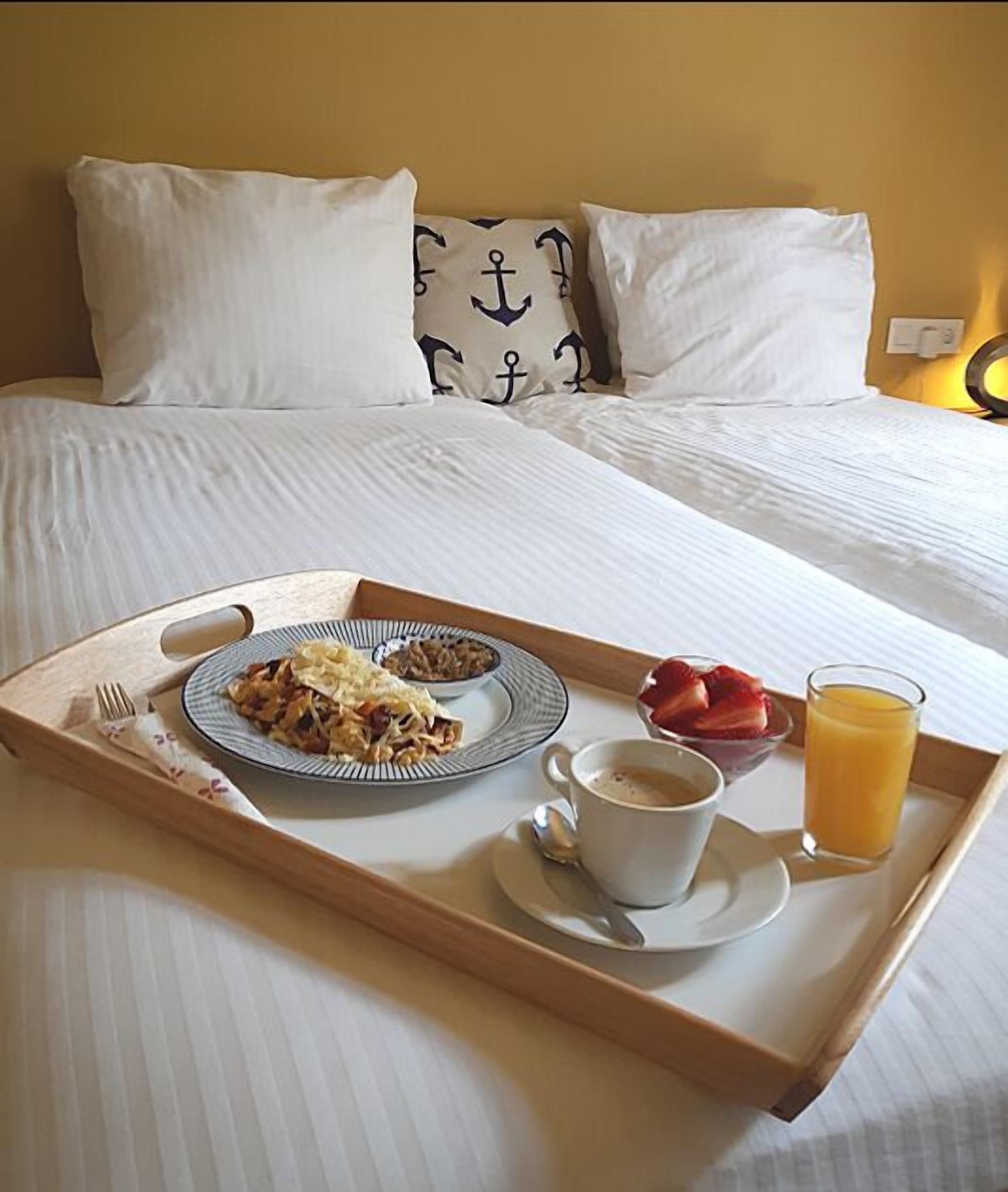 A breakfast tray on a bed with white bedding, a plate of food, a cup of coffee, a glass of orange juice, and a fork.
