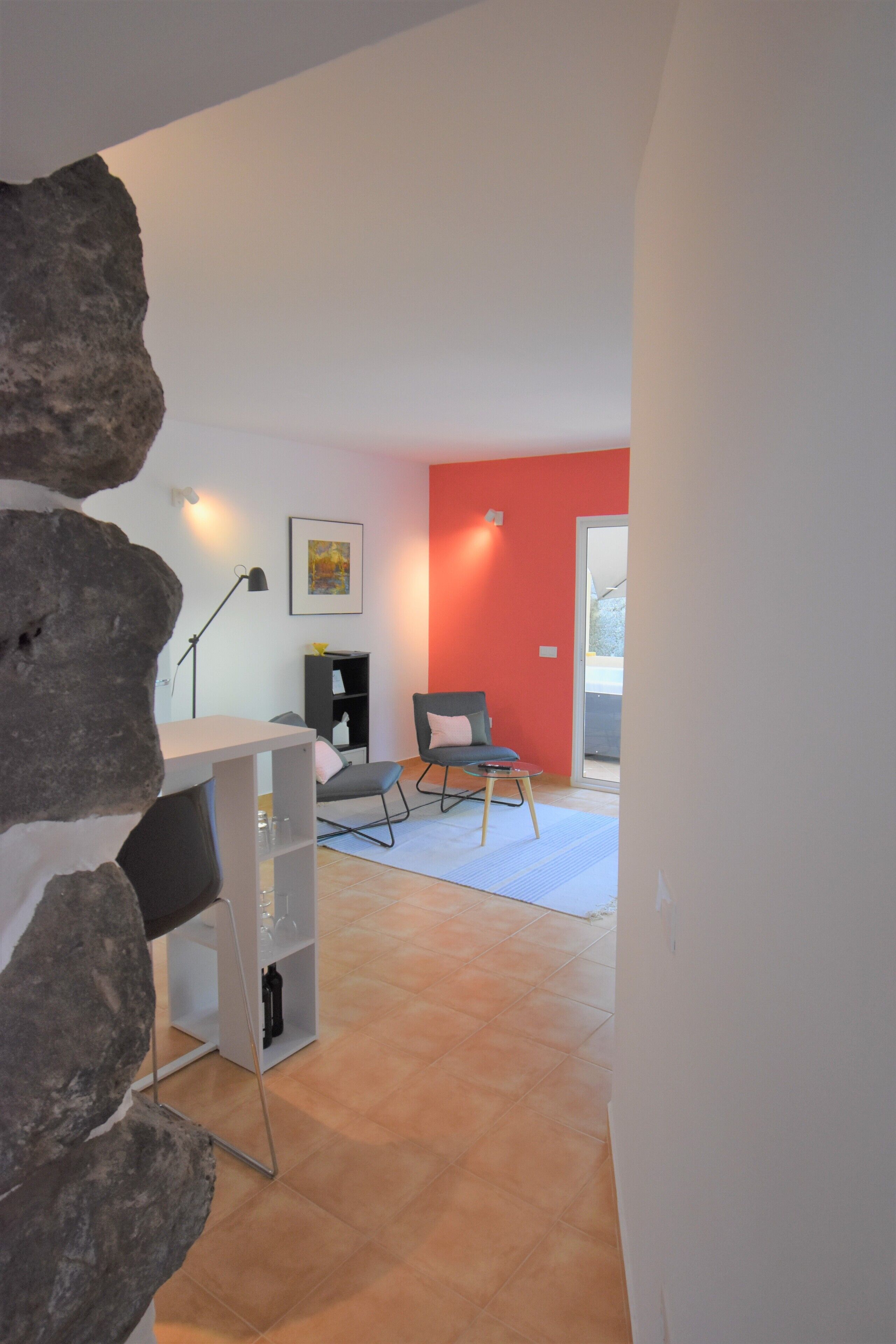 Ein modernes Wohnzimmer mit roter Akzentwand, einem grauen Sofa, einem kleinen Tisch und einem Bücherregal.