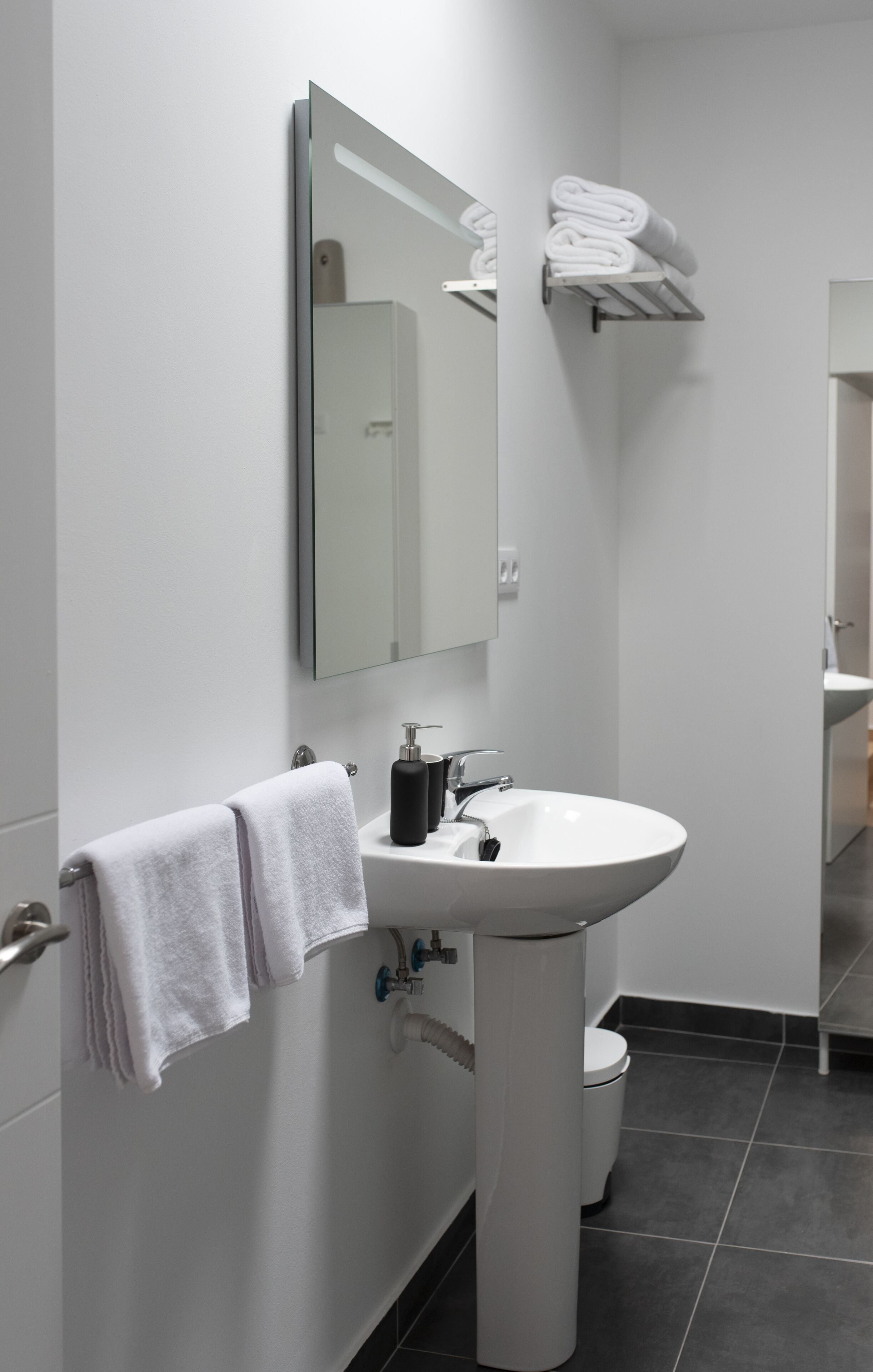 A modern bathroom with a white sink, a mirror, and a towel rack.