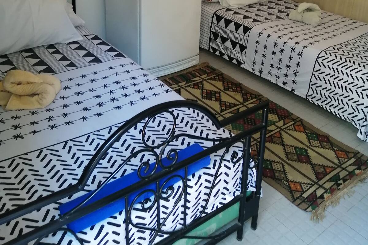 Una habitación con dos camas, un refrigerador blanco pequeño y un espejo en la pared.