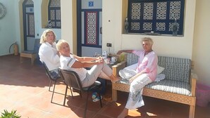 Un patio con un banco y sillas de madera, suelo de baldosas y una puerta con un número.
