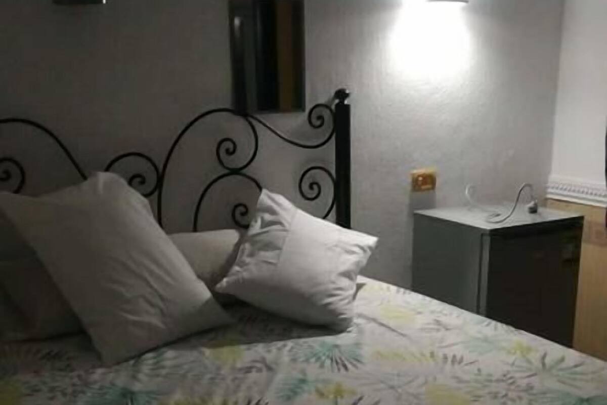 Una cama con una colcha estampada, una mesita de noche con lámpara y un espejo fijado en la pared.