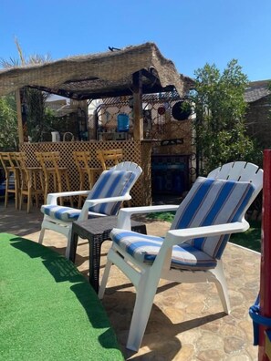 Un área de estar al aire libre con sillones reclinables a rayas blancas y azules, una mesita y una estructura de paja.