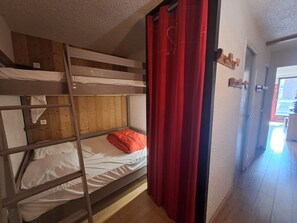 A bunk bed room with a red curtain, wooden paneling, and a door leading to another room.
