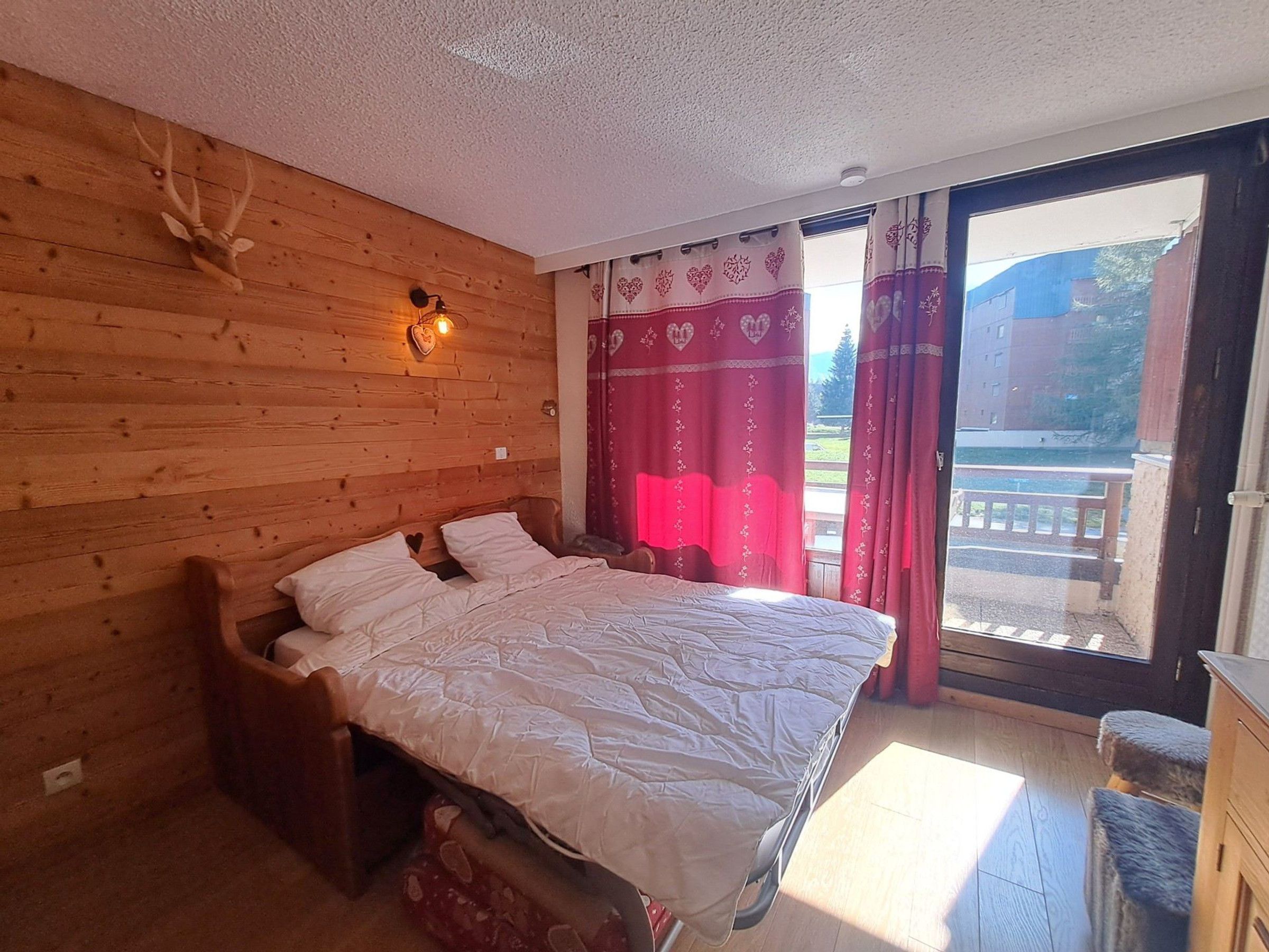 Habitación con paneles de madera, una cama, una lámpara de pared y vistas a través de una puerta corrediza de cristal.