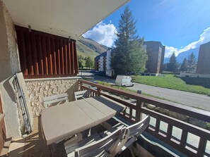 A balcony with a table and chairs, overlooking a street with buildings and a mountain in the background.