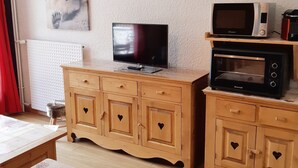 Habitación con un armario de madera con recortados en forma de corazón, un televisor y un microondas.